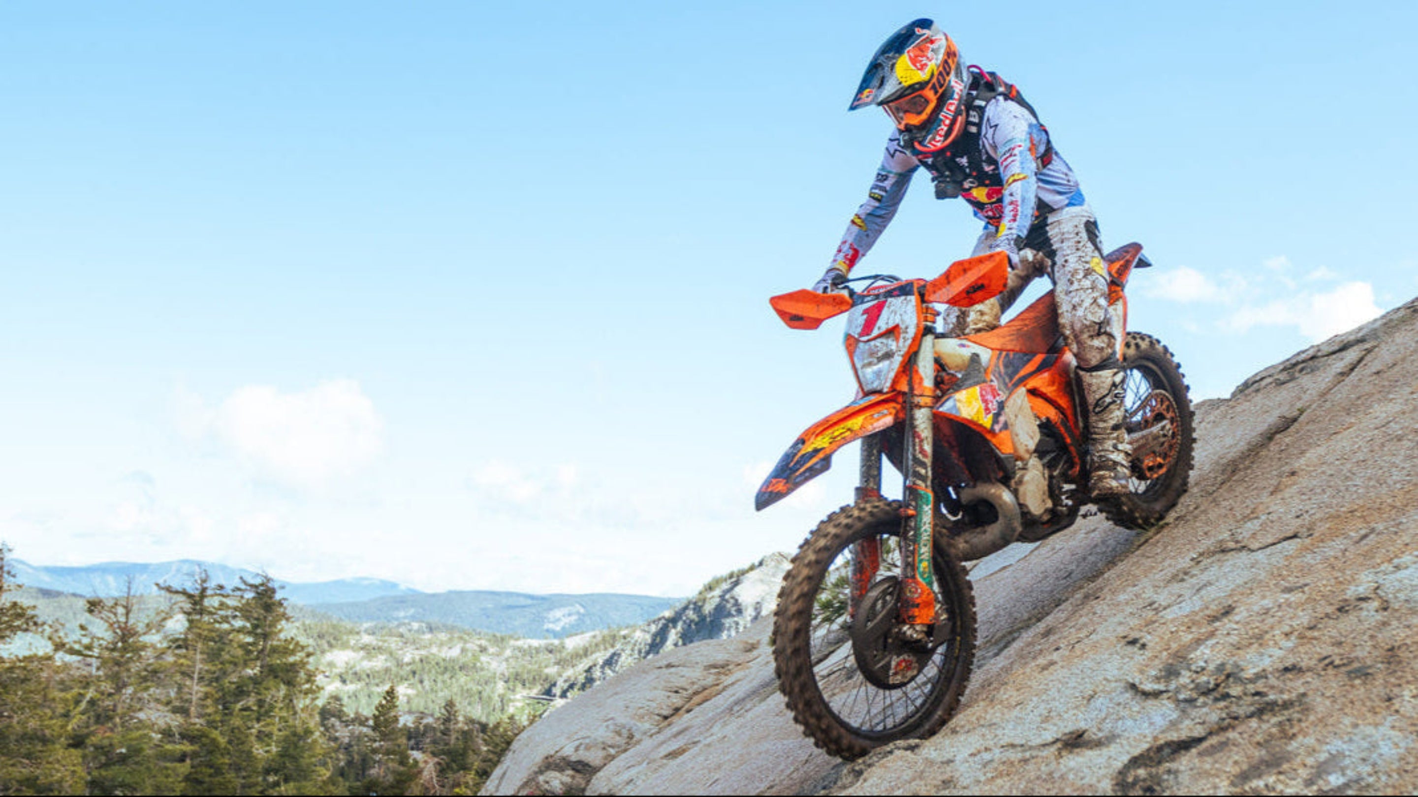 Person riding a dirt bike on a rocky hillside with a clear blue sky.